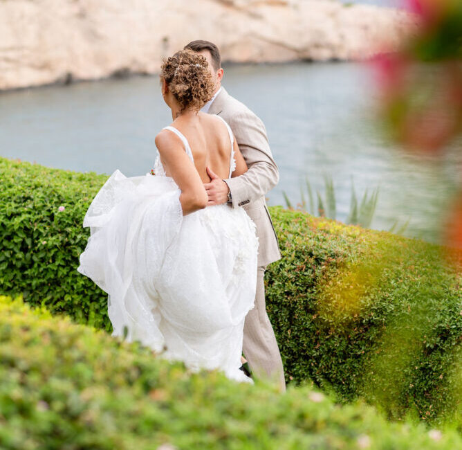 Bride and groom embrace by scenic coastal cliffs and water, romantic wedding portrait in garden setting