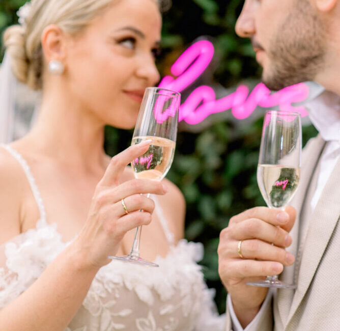 Bride and groom toasting with champagne glasses at wedding reception, green foliage background